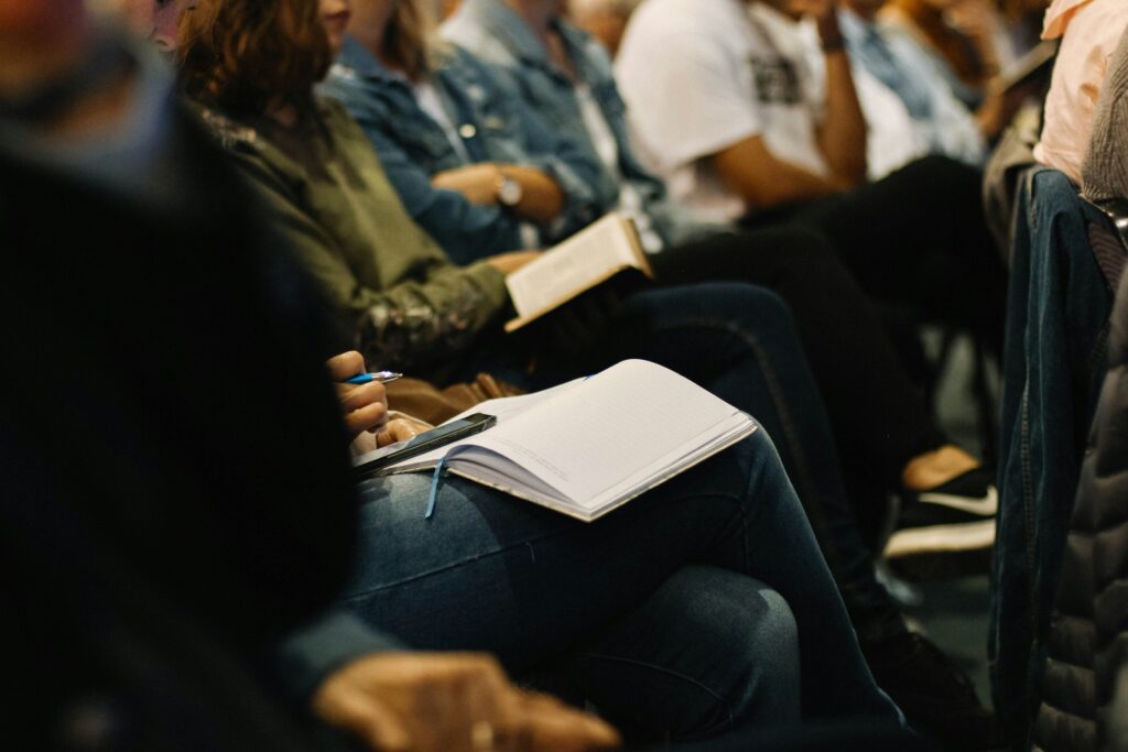 A row of people in a conference having their notebooks on their laps and writing notes.