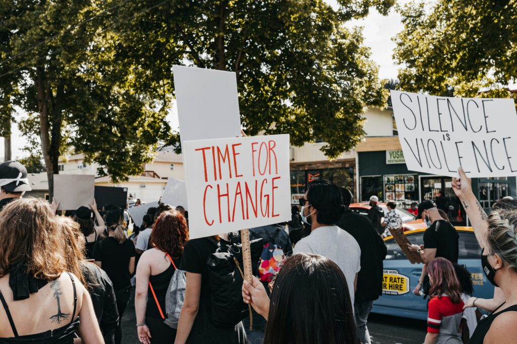 A protest with signs saying "Time for a change" and "Silence is Violence".