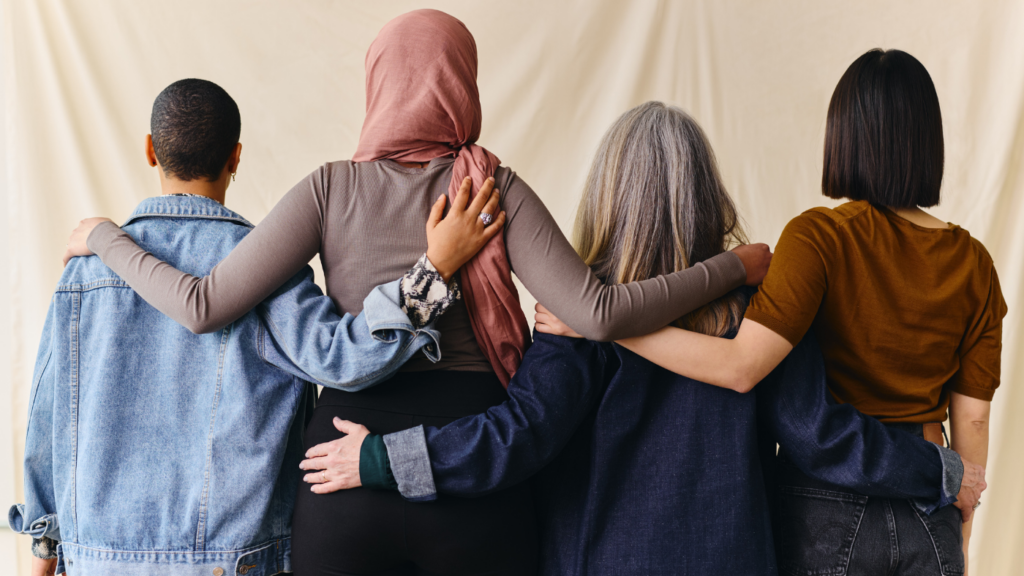 Four women standing in line with arms around each other's shoulders.