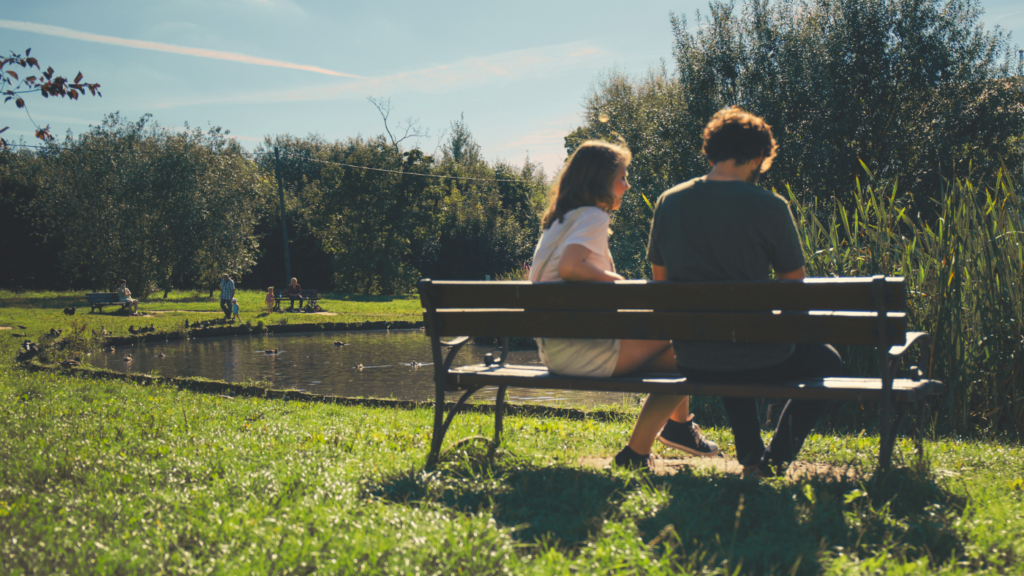 two people sitting next to a pond during a sunny day