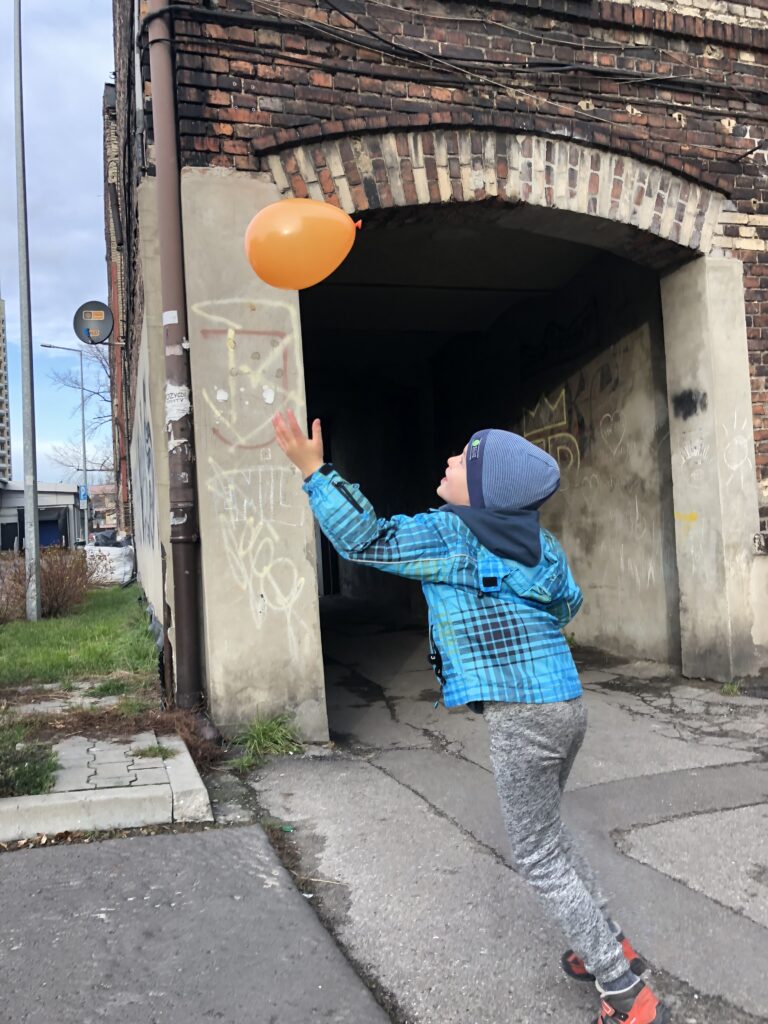 a boy in a blue jacket chasing after an orange baloon