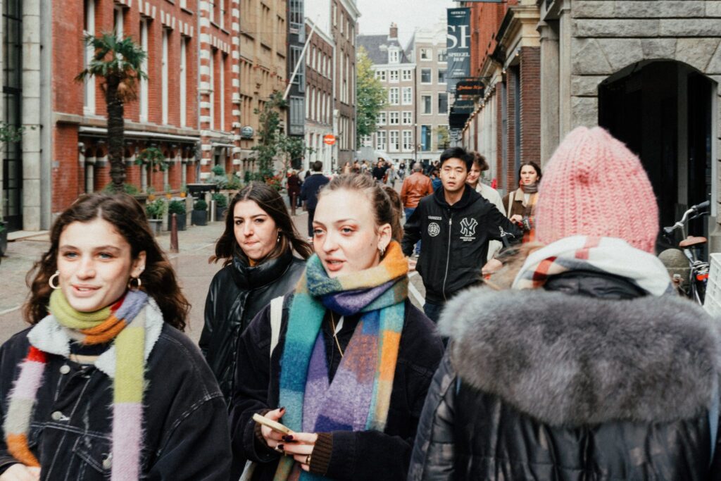 The photo is showcasing a street full of people with young women in the foreplan wearing winter clothing and colourful scarfs