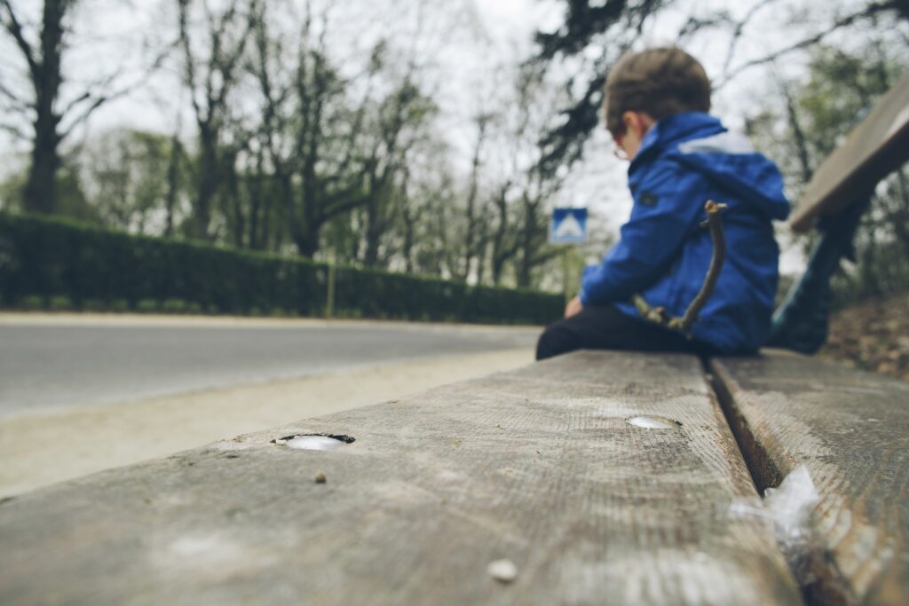 a child sitting alone on a bench holding a stick in his hand